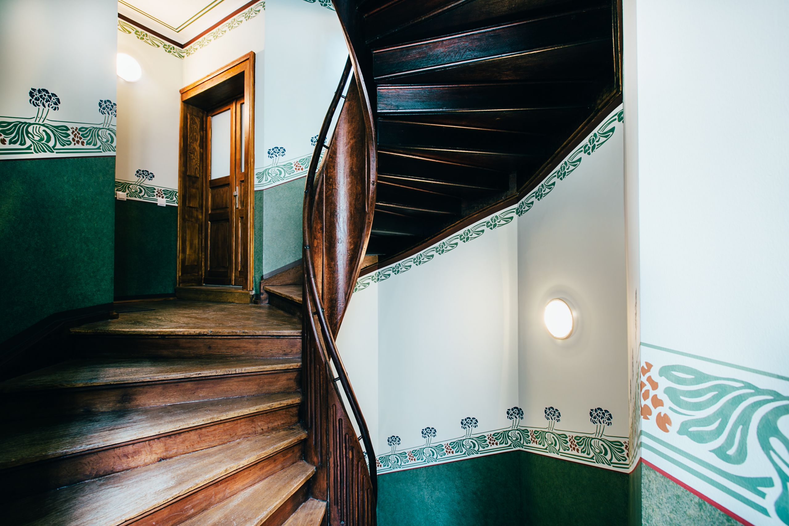 Historisches Treppenhaus mit Holztreppe und dekorativen Wandfliesen in einem Altbau.