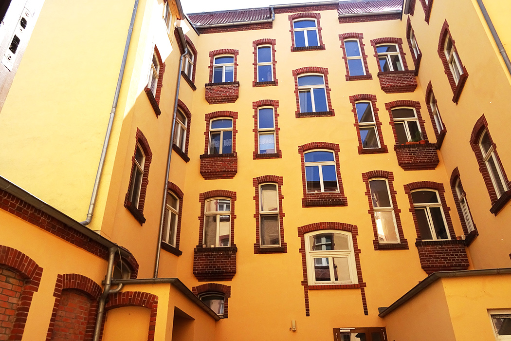 Historischer Innenhof eines Altbaus mit gelber Fassade und roten Backsteinakzenten, sonnige Atmosphäre und klassische Architektur.