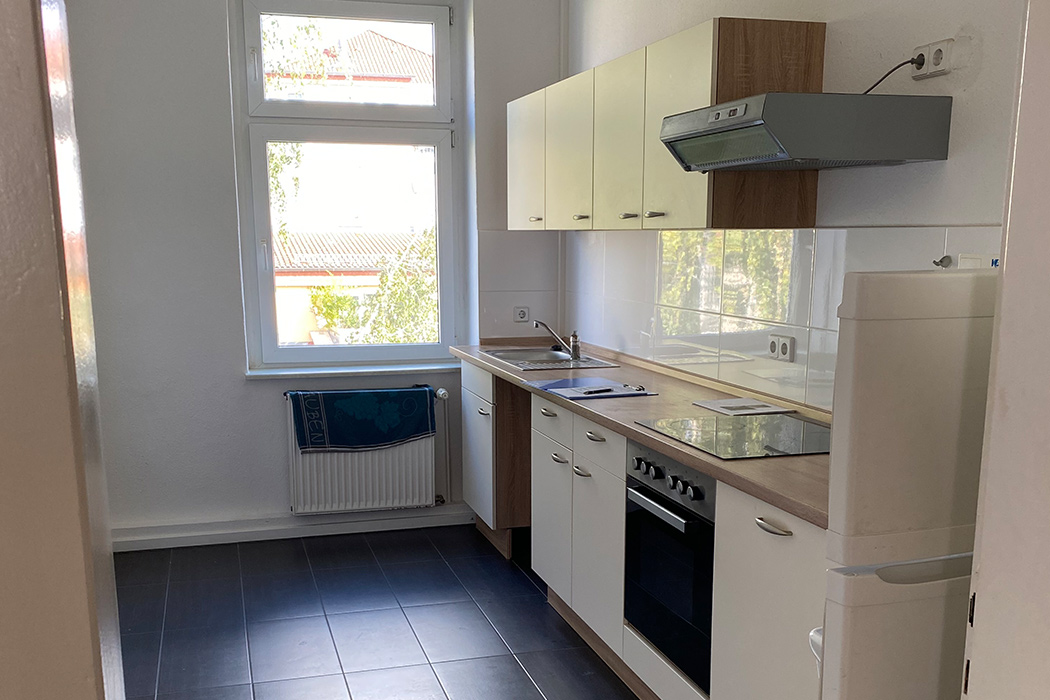 Helle, moderne Küche mit Einbauküche, Herd, Dunstabzugshaube und großem Fenster, gefliest in Schwarz-Weiß.