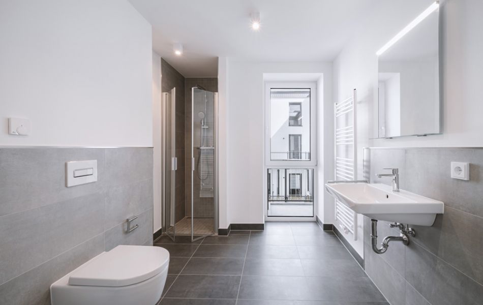 Modernes, helles Badezimmer mit bodengleicher Dusche, großen Fliesen, Wand-WC und Fenster für natürliche Belüftung.