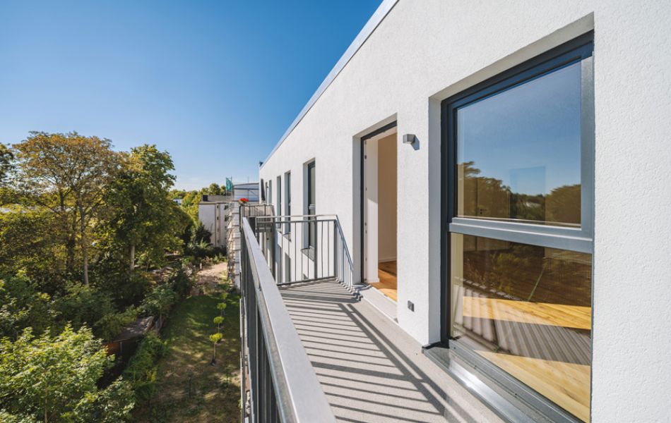 Moderner Balkon mit Blick ins Grüne, helle Fassade, große Fenster und offene Architektur für lichtdurchflutetes Wohnen.