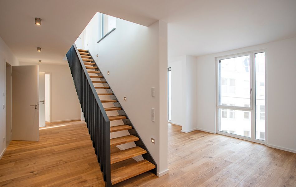 Moderne Maisonette-Wohnung mit offener Holztreppe, großen Fenstern und hellem Parkettboden für ein stilvolles Wohnambiente.
