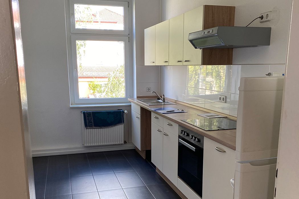 Helle, moderne Küche mit Einbauküche, Herd, Dunstabzugshaube und großem Fenster, gefliest in Schwarz-Weiß.