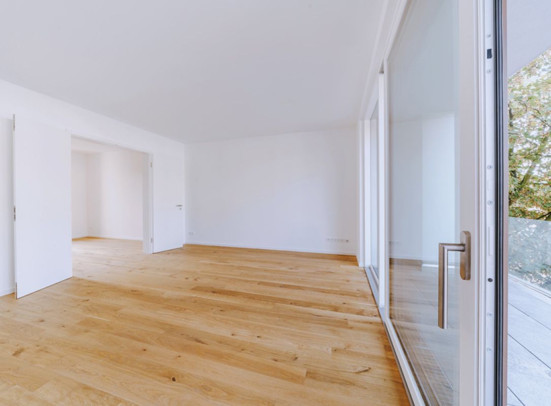 tilvolles Altbaugebäude mit hellen Fassaden, großen Fenstern und grünen Bäumen, im Sonnenlicht fotografiert.