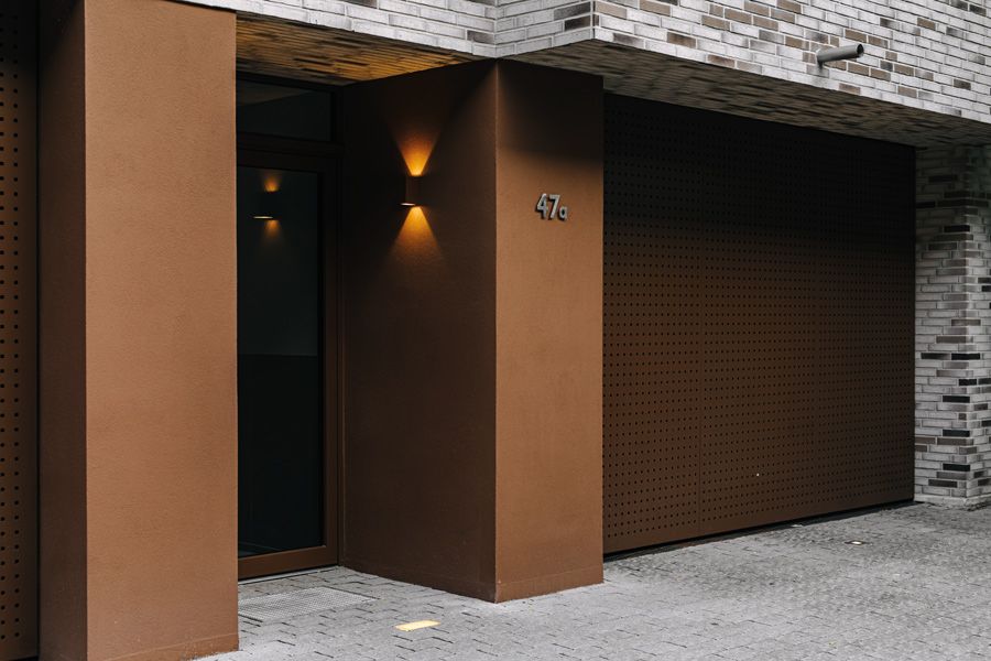 Moderne Hauseingangstür mit brauner Fassade, stilvoller Beleuchtung und minimalistischer Architektur.