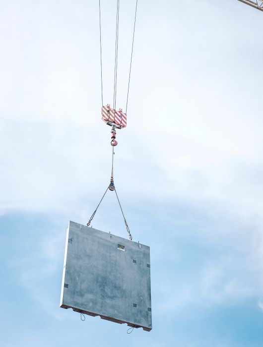 Baukran hebt massive Betonwand in die Luft, moderner Hochbau mit präziser Konstruktionstechnik unter klarem Himmel.