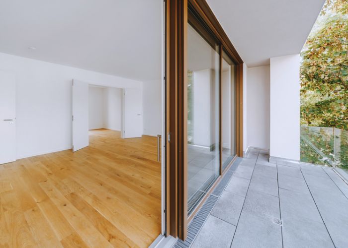 Leerer, heller Raum mit Holzboden und großer Glasfront zum Balkon mit Stadtblick.