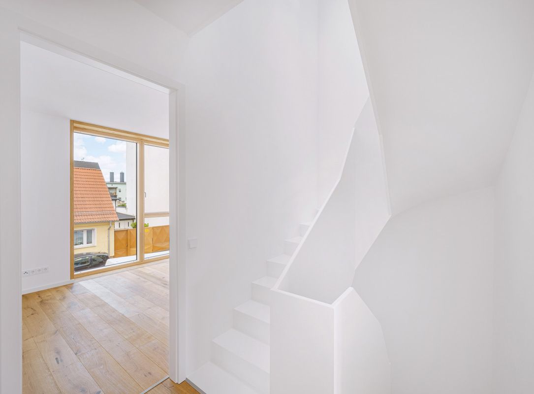 Modernes weißes Wohngebäude mit großen Fenstern und offenen Balkonen, minimalistische Architektur vor klarem blauem Himmel.