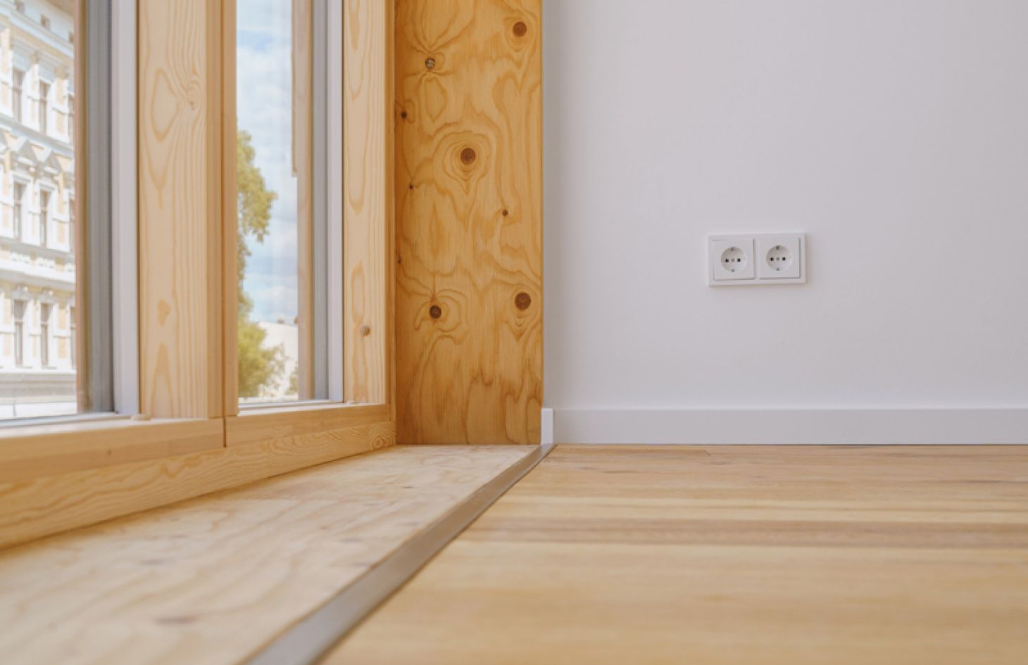 Detailaufnahme eines modernen Innenraums mit Holzfenster, Parkettboden und weißen Wänden für eine natürliche Wohnatmosphäre.