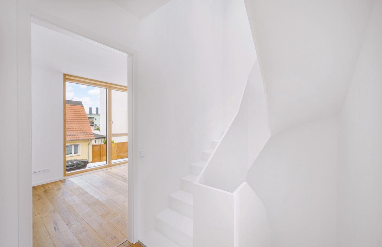Helles, minimalistisches Treppenhaus mit weißem Design, großem Fenster und Holzfußboden für modernes Wohnen mit viel Tageslicht.