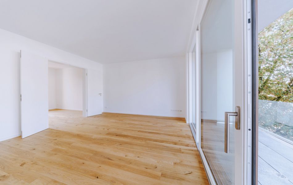 Helles, modernes Wohnzimmer mit Parkettboden, großen Fenstern und offener Raumgestaltung mit Zugang zum Balkon.