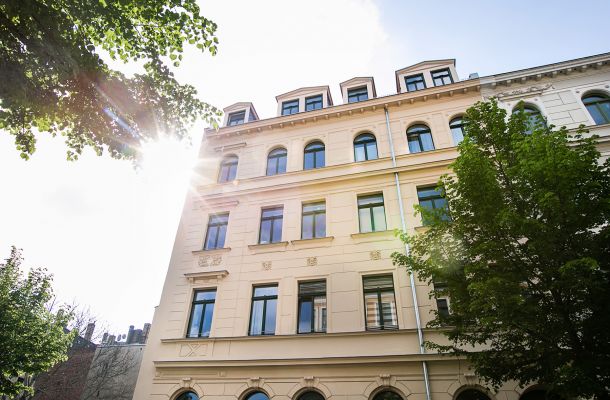 Saniertes Altbau-Gebäude in der Sonne mit grünen Bäumen im Vordergrund.