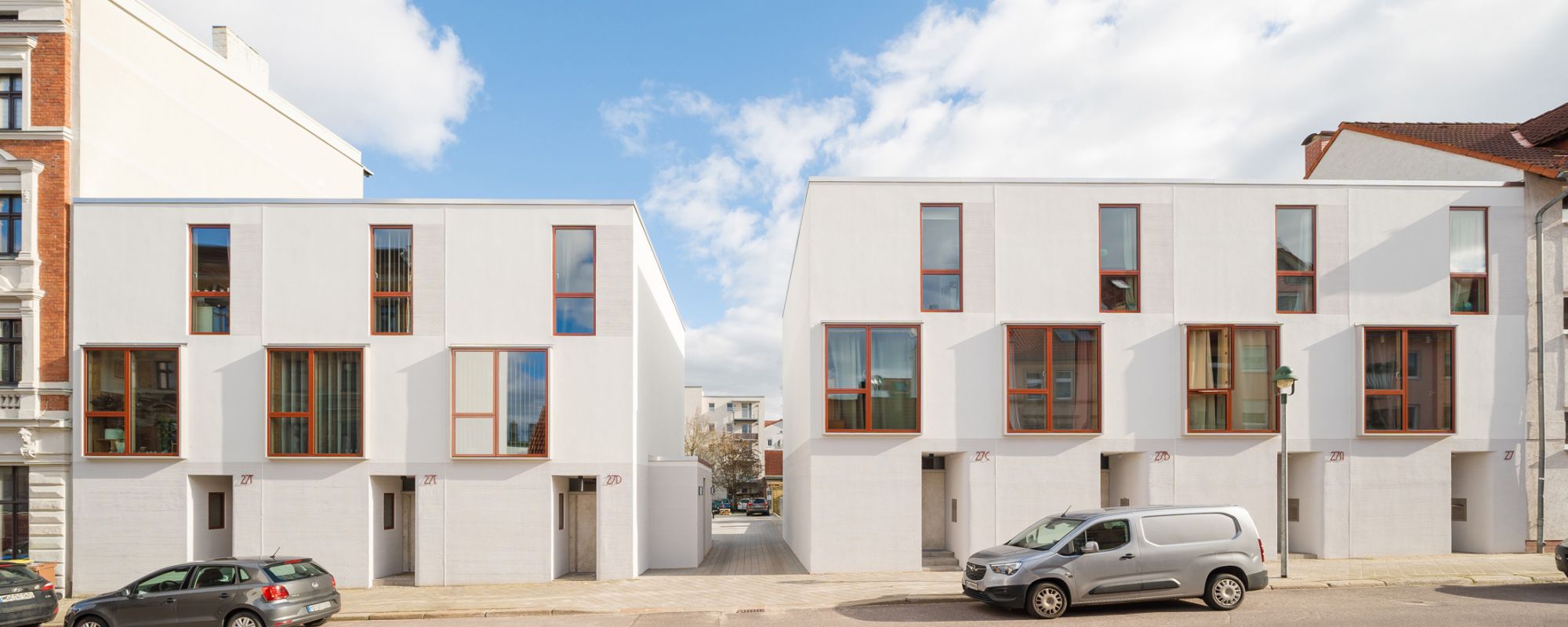 Modernes Wohngebäude mit großzügigem Balkon, helle Fassade, Stadtansicht mit Kirche im Hintergrund bei Sonnenschein.