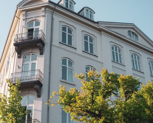 Elegantes historisches Gebäude mit Balkonen und grünen Bäumen, aufgenommen bei klarem Himmel und warmem Sonnenlicht.
