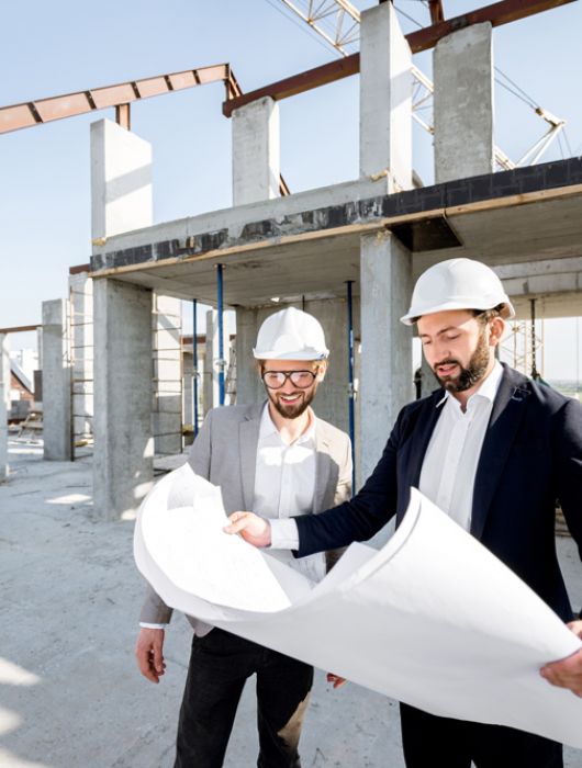 Architekten mit Bauplänen auf einer Baustelle, tragen Schutzhelme und planen den Fortschritt eines modernen Bauprojekts.